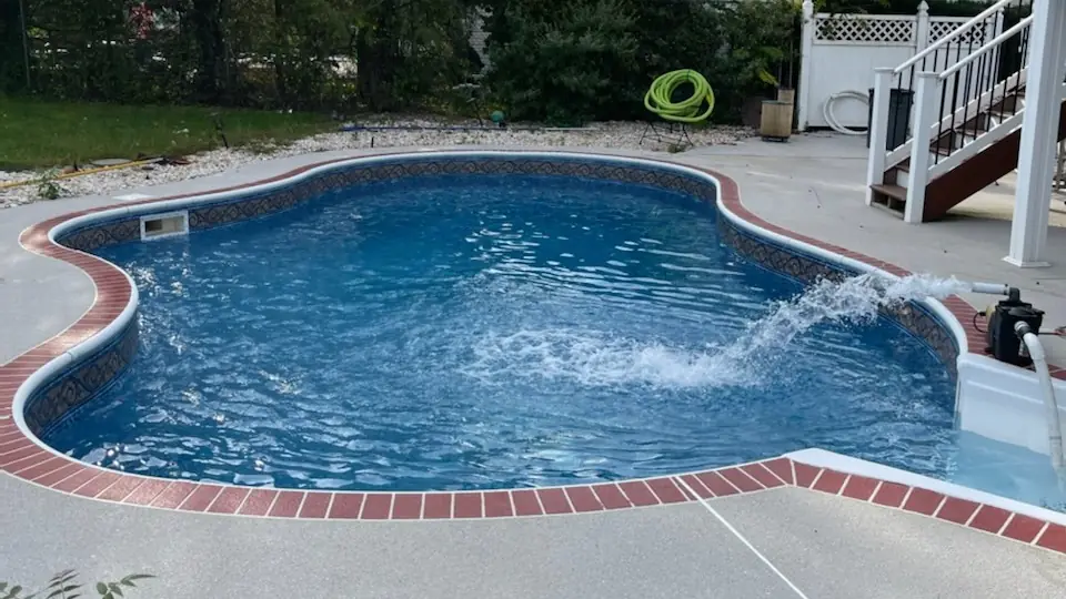A finished kidney-shaped pool with red brick coping, water filling from the right