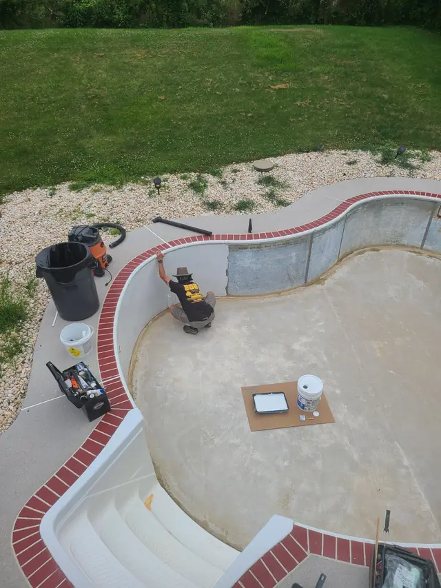 Crew member painting a prepped pool wall with tools laid out on the pool floor